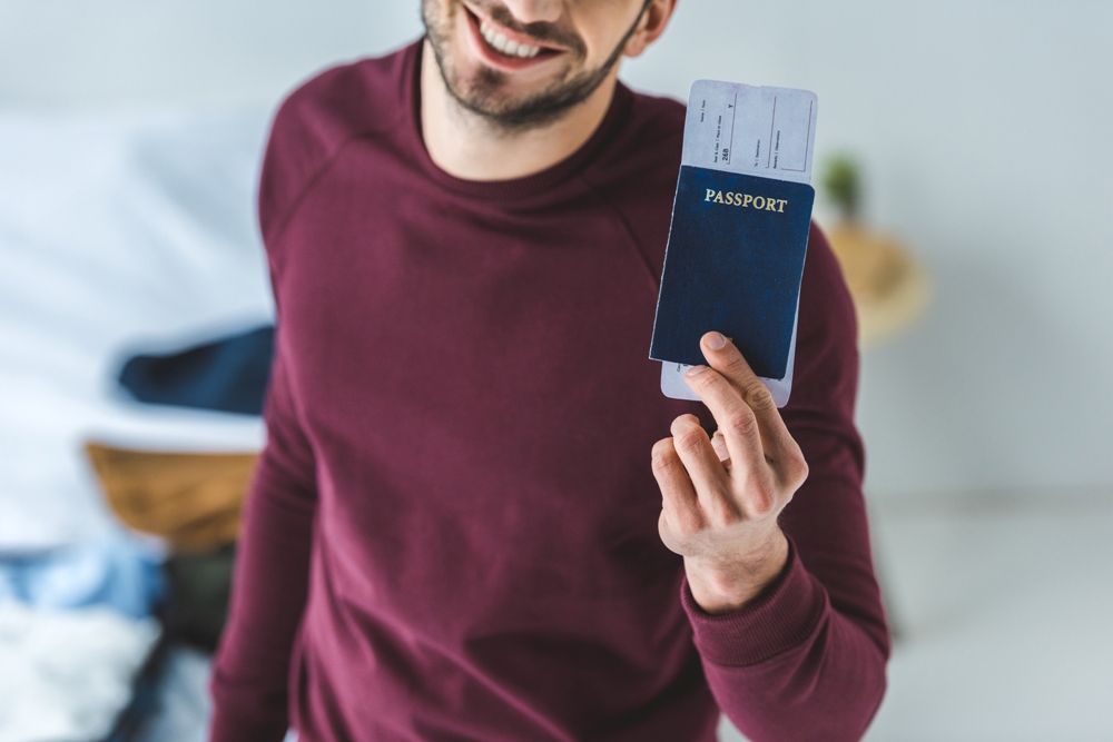 cropped view of smiling man holding passport and air ticket